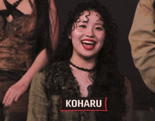 a woman with long curly hair is smiling in front of a sign that reads koharu