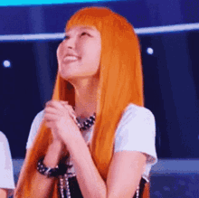 a woman with orange hair is smiling with her hands folded .