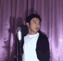 a young man stands in front of a microphone in front of a purple curtain
