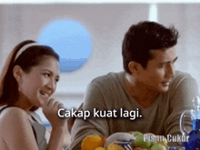 a man and a woman are sitting at a table with the words cakap kuat lagi in the corner