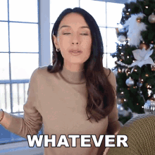 a woman is standing in front of a christmas tree and says " whatever "