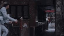 a woman in a denim jacket is jumping in the air in front of a restaurant