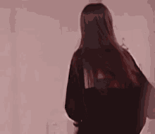 a young woman with long hair is standing in front of a pink wall and smiling .