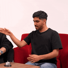 a man in a black shirt is sitting in a red chair talking to another man