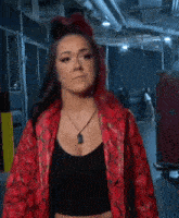 a woman in a red jacket and black top is standing in a room .