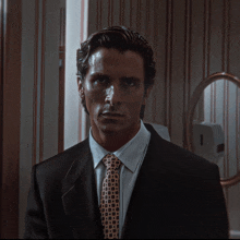 a man in a suit and tie stands in front of a bathroom mirror