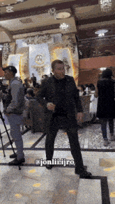 a man in a suit is dancing in a room with jonliiijro on the bottom