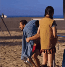 a woman in a plaid skirt is standing next to a man in a denim shirt on the beach