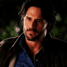 a man with a beard wearing a leather jacket and a blue shirt