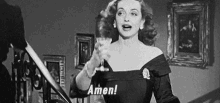 a woman in a black dress is holding a wine glass and saying amen .
