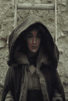 a woman in a hooded cape is standing next to a ladder .