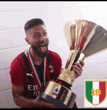 a man wearing a red fly emirates shirt is holding a trophy