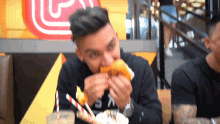 a man in a black shirt with the letter s on it eating a hamburger