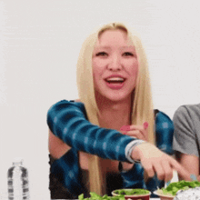 a woman with blonde hair is sitting at a table with a salad and a bottle of water
