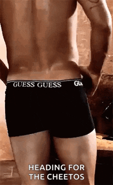 a shirtless man wearing black guess boxer shorts is standing in a bathroom .