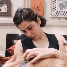 a woman in a black tank top is playing with a dog in front of a framed picture of a man