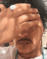 a man with curly hair and a beard is covering his face with his hand .
