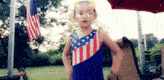 a little girl wearing an american flag outfit and sunglasses stands in front of an american flag