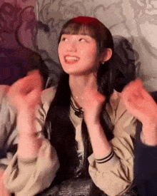 a young girl is sitting on a couch with her hands in the air and smiling .