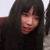 a girl with long black hair and bangs is smiling and looking at the camera .