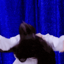 a woman in a white shirt is standing in front of a blue curtain with her arms outstretched .