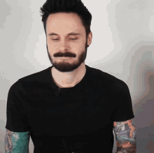a man with a beard and tattooed arms is wearing a black shirt
