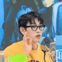 a young man wearing glasses and a yellow sweater is giving a thumbs up sign .