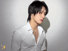 a young man in a white shirt and necklace is standing in front of a white wall .