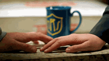 a person touching another person 's hand with a blue mug in the background