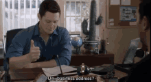 a man is giving a thumbs up while sitting at a desk and talking to another man who is asking about his business address