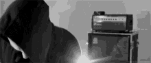 a black and white photo of a person in a hooded jacket standing in front of a stack of speakers .
