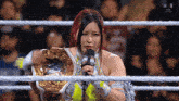 a woman in a wrestling ring is holding a microphone and a championship belt .