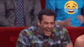 a man in a floral shirt is laughing with tears coming out of his eyes while sitting in a theatre .