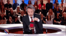 a man in a suit and tie is holding a red box in front of a crowd that is watching tmc