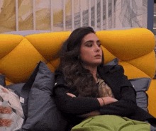 a woman is laying on a yellow couch with her arms crossed and looking at the camera .