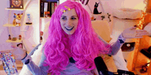 a woman wearing a pink wig is smiling and sitting in front of a microphone