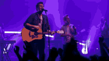 a man sings into a microphone while another man plays a guitar