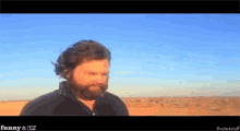 a man with a beard is standing in the desert with a blue sky behind him and the words funny & die on the bottom