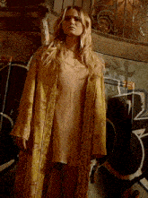 a woman in a yellow robe is standing in front of graffiti