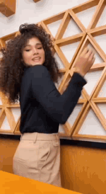 a woman with curly hair is dancing in a room in front of a wooden wall .