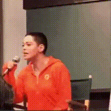 a man in an orange hoodie is holding a microphone