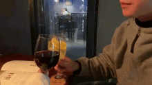 a person is sitting at a table holding a glass of wine and a glass of lemonade .