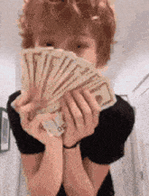 a young man is holding a bunch of money in front of his face .