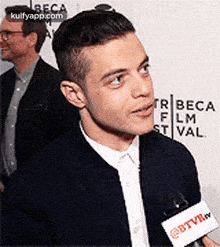 a man is talking into a microphone while standing on a red carpet at a film festival .