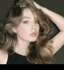 a woman in a black tank top holds her hair