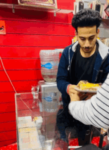 a man holding a plate of food in front of a water cooler