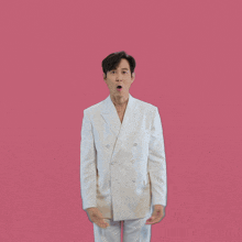 a man in a white suit making a heart with his hands