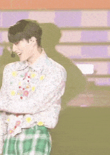 a young man in a floral shirt and green plaid skirt is standing on a stage with his arms crossed .