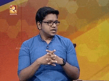 a man wearing glasses and a blue shirt is sitting in front of a colorful background and talking .