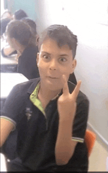 a boy in a black polo shirt is making a funny face and giving the middle finger